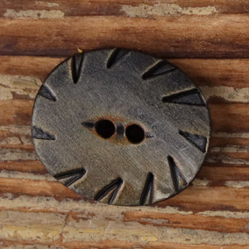 Oval two-hole horn button in grey with carved radial pattern and two holes.