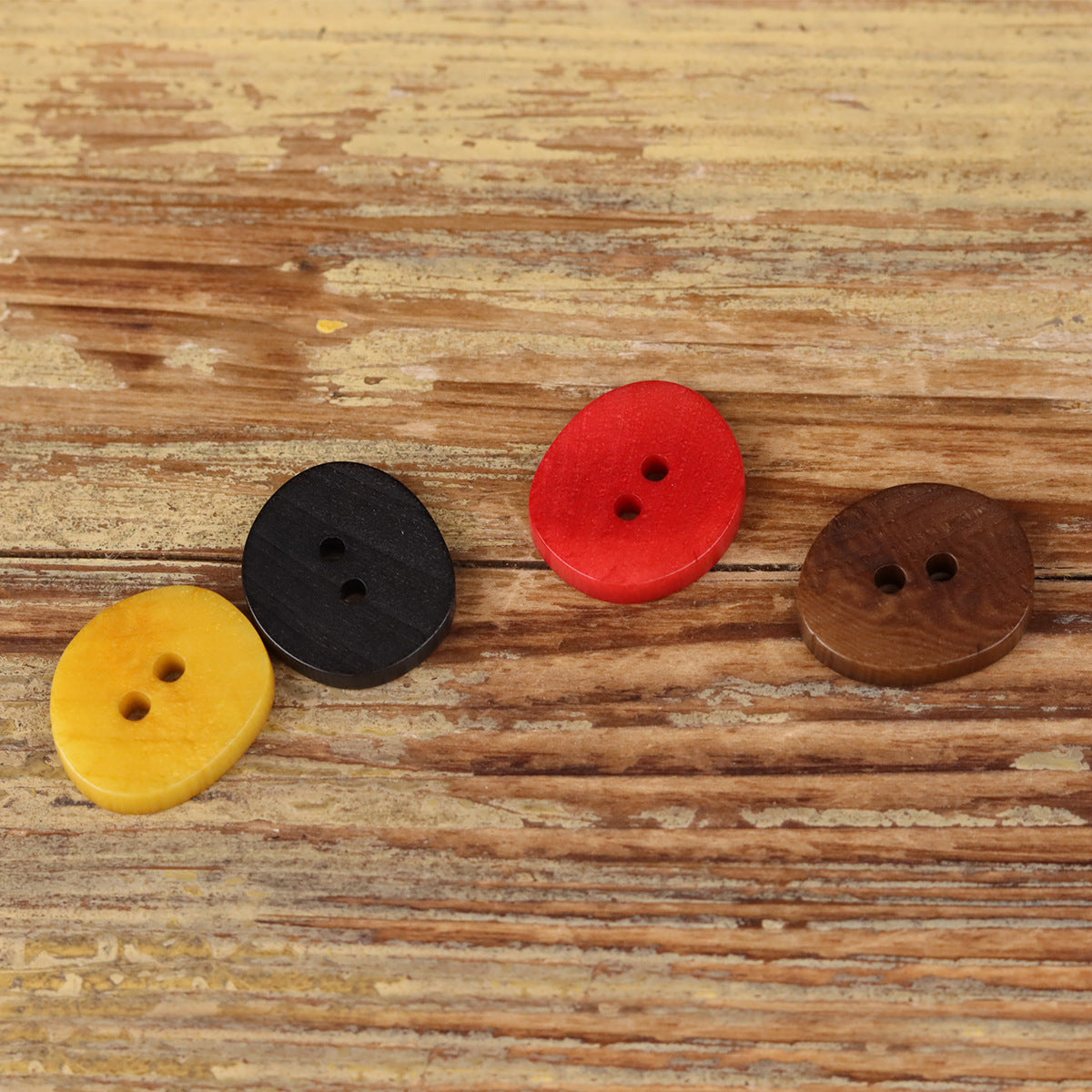 Assorted natural 2-hole buttons in black, red, yellow, and brown on wood.