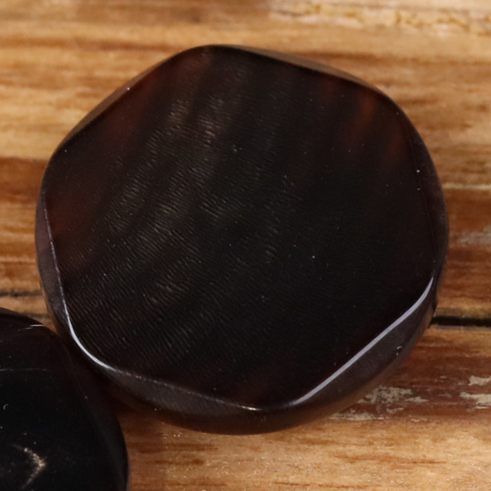 Buffalo horn button in dark color with irregular edge and hidden eye detail