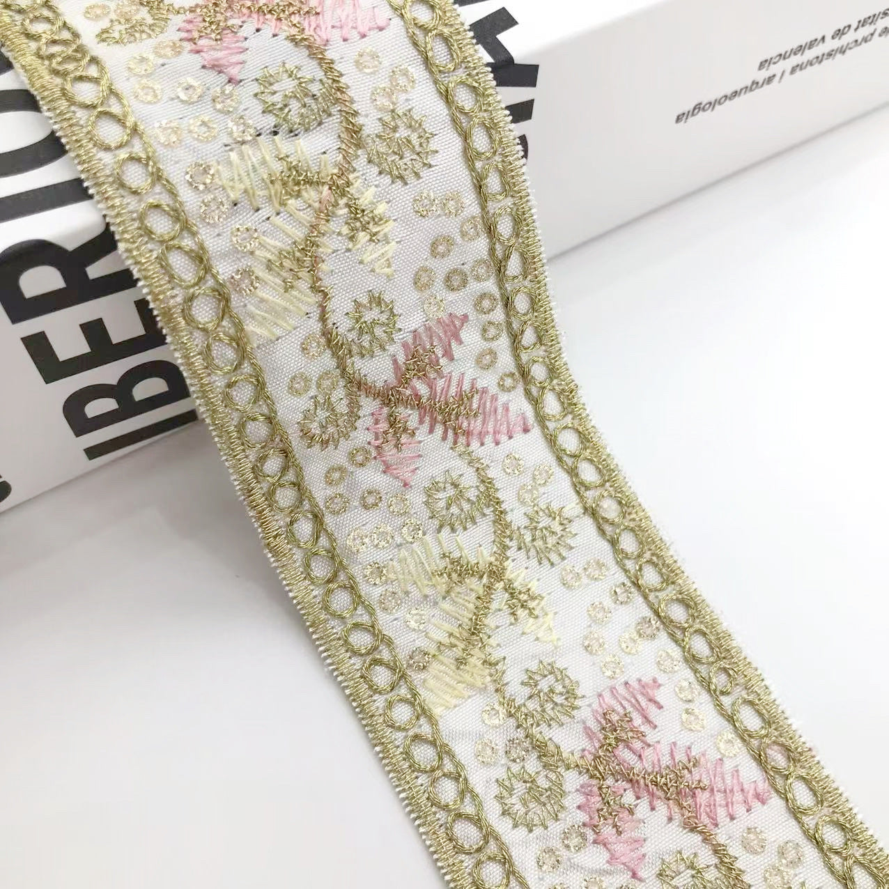 Goldene Bortenstickerei mit rosa Akzenten und Kordelösen entlang der Kante