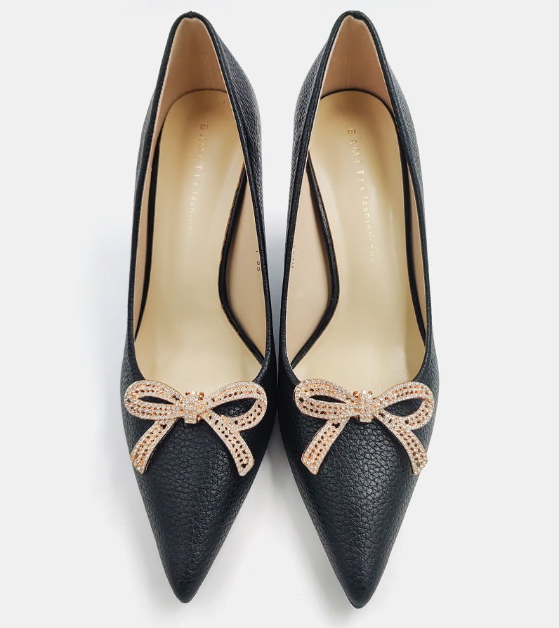 Gold-tone rhinestone bow detail on black pointed-toe high heels, bow centered on vamp