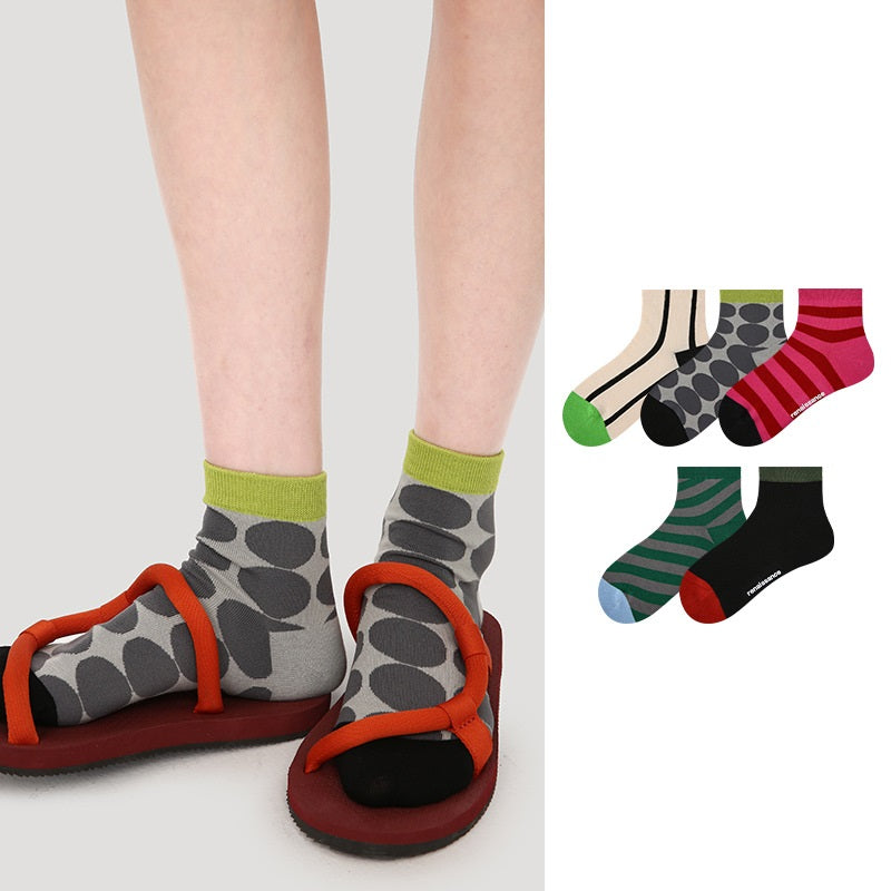 Dünne Sport-Socken am Fuß: graue Punktmuster mit grünem Bündchen und schwarze Socke mit Streifen