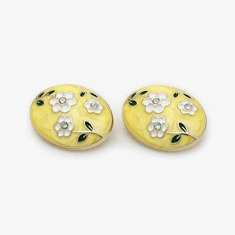 Oval floral enamel metal button, yellow with white flowers, green leaf accents, gold edges