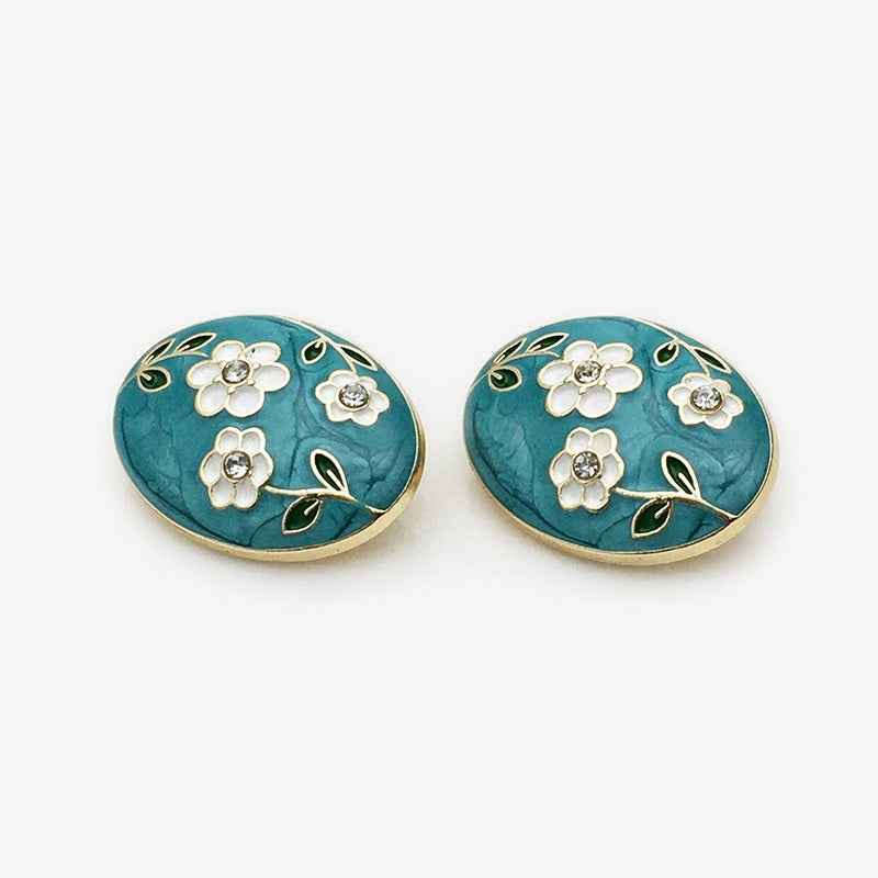Oval floral enamel metal button, teal with white flowers, green leaf accents, gold edges